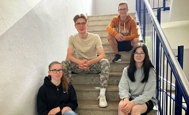 News- Bild: Vier Teilnehmer*innen posieren auf einer Treppe sitzend