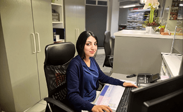 News- Bild: Frau posiert in Arbeitskleidung vor einem PC sitzend für das Foto