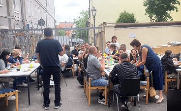 News- Bild: Viele Personen sitzen im Freien an zwei Tischreihen 
