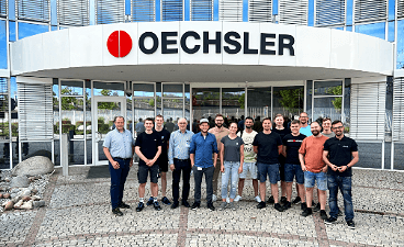 15 Personen posieren vor dem Oechsler- Gebäude stehend.