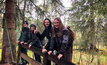 News- Foto: Vier Jugendliche posieren lachend nebeneinander in einem Wald stehend