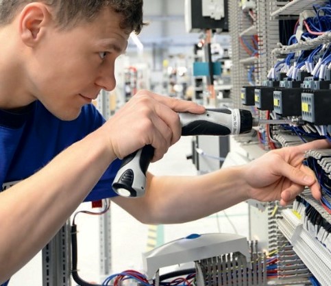 Techniker führt Wartungsarbeiten an einem geöffneten Schaltschrank mit einem Schraubendreher durch.