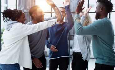 Teaser: Eine diverse Gruppe von Menschen geben sich lachend High-Fives und feiern gemeinsam einen Erfolg.