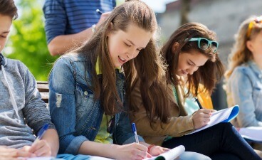 Jugendliche sitzen zusammen und schreiben konzentriert in ihre Hefte.