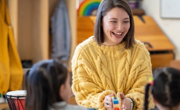 Einer Erzieherin sitzt Kindern gegenüber und lacht.