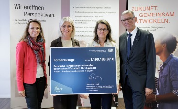 Förderscheckübergabe für die Anerkennungsberatung Das Bild zeigt vier Personen, die in einem Raum stehen und einen Förderbescheid über 1.199.188,97 € präsentier Im Hintergrund sind Plakate mit den Worten „Wir eröffnen Perspektiven“ und „Zukunft. Gemeinsam. Entwickeln.“ zu sehen.